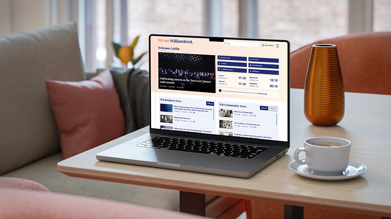 An open laptop on a coffee table in a livingroom featuring the William Reed Intranet landing page